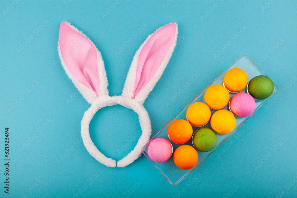 Colorful handmade Easter eggs and rabbit ears to play with. Top view of an open transparent box. Isolated on a blue background. Preparing for Easter.