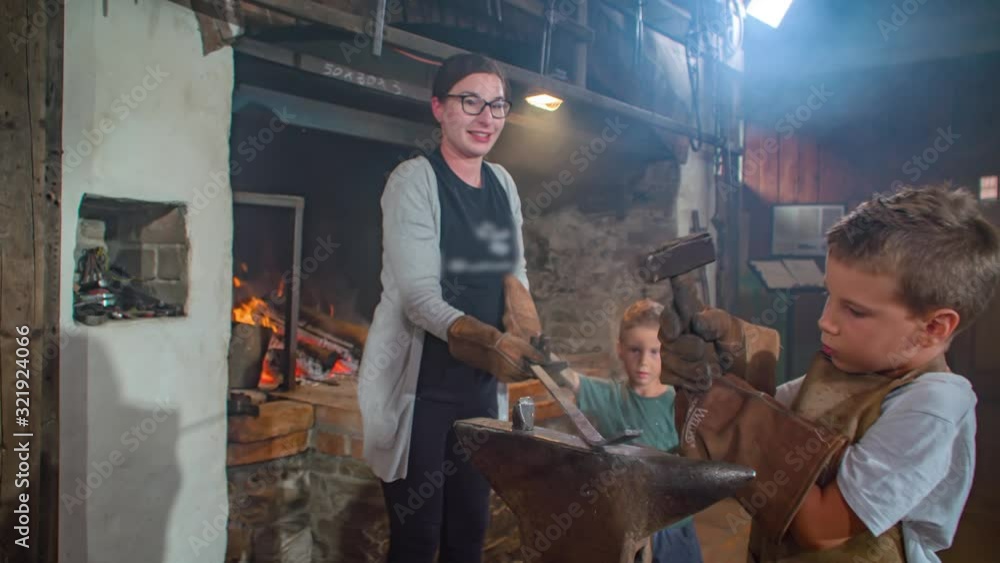 Little boy with gloves and apron hitting hard a piece of hot iron with a hammer. Slow motion Little boy with gloves and apron hitting hard a piece of hot iron with a hammer. Slow motion