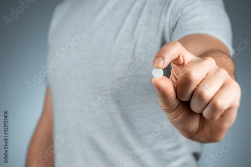 Close-up male hands holding a white pill, taking medication, treatment, gray background. Medical theme, vitamins, health care.