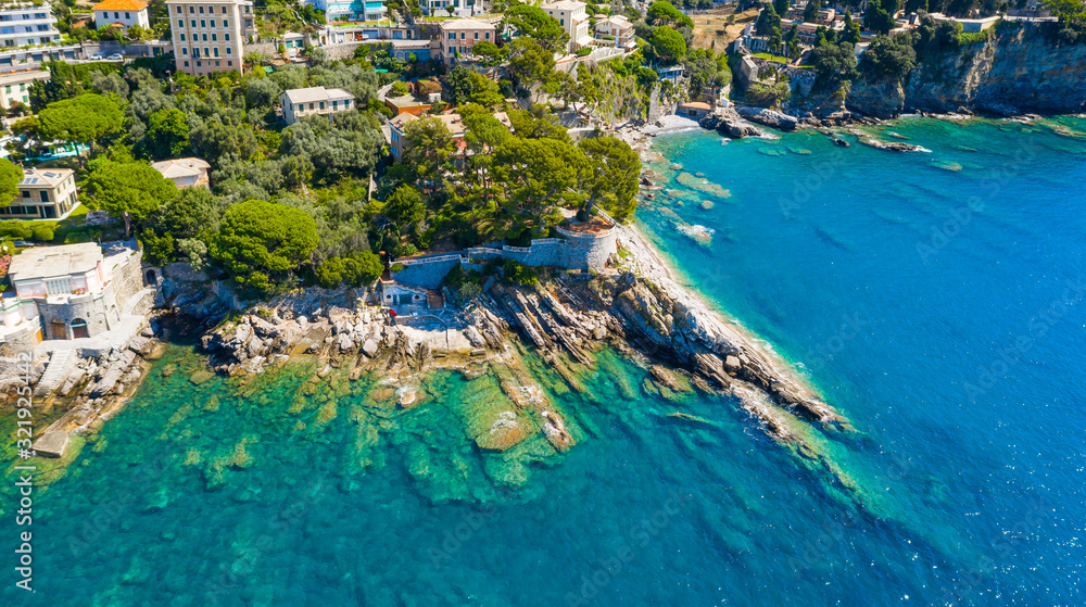 Fototapeta premium Aerial view on the city with colorful houses located on the rocky coast of ligurian sea, Camogli near Genoa, Italy. Rocky Coastline is washed by turquoise blue water.