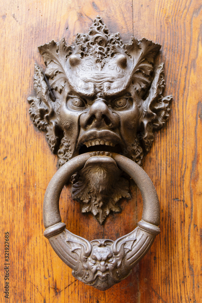 artistic large face as a door knocker on an antique door in Italy