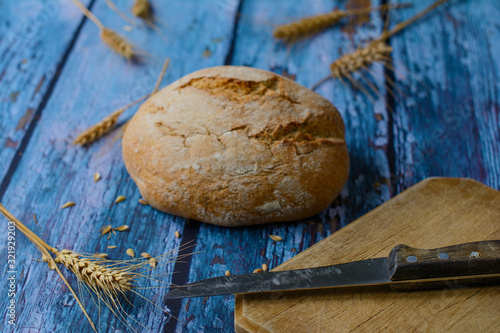 An old knife is on the wooden cutting board. Traditional Vojvodinian round bread called cipovka. Wheat ears, grains. Selective focus on the knife. photo