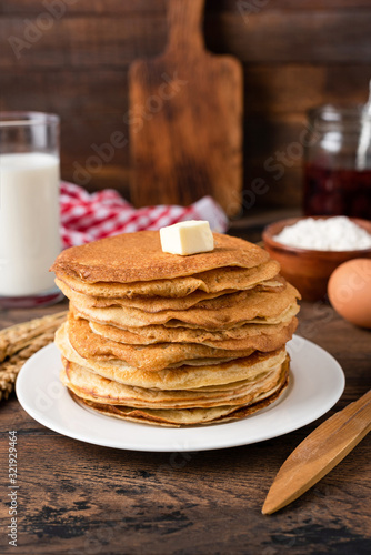 Stack of thin crepes, blini with butter on white plate. Maslenitsa, Shrove Tuesday concept. Vertical orientation, rustic style