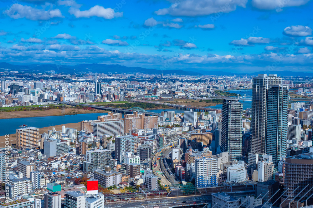 Japan. Panorama of Osaka from a height. Japanese urban landscape. Bridges over the Yodo river. Road and railway bridge. Big city under the sky with clouds. Osaka against the mountains. Town houses.