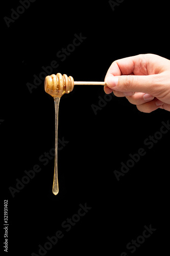 A spoon of honey in hand on a black background. Dripping fresh honey.