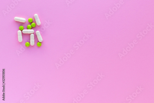 Green pills and white capsules isolated on pink background. Woman health. Epidemic, painkillers, healthcare and treatment concept. Flat lay. 