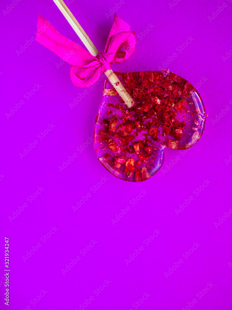 Fototapeta premium Red heart-shaped lollypop shot over purple background, minimalist concept for Valentines Day, Mothers Day. Love creative hearts shape, minimal simple design for wedding, anniversary invitations