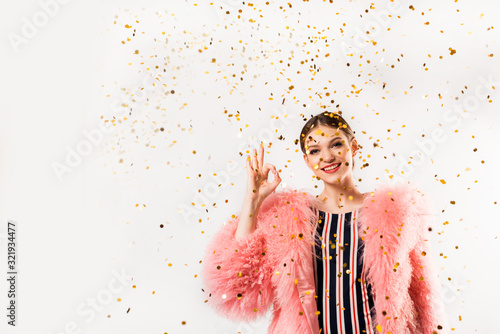 Funny woman celebrating with air balloons isolated white. Shows hand okay. in a pink fur coat, golden tinsel.Vivid emotions, surprise and joy, laughter and scream.Birthday holiday party photo