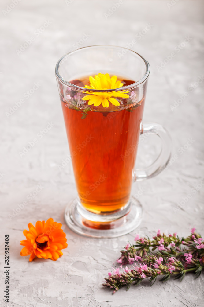 Glass of herbal tea with calendula and hyssop on a gray concrete background. Side view, close up. Glass of herbal tea with calendula and hyssop on a gray concrete background. Side view, close up.