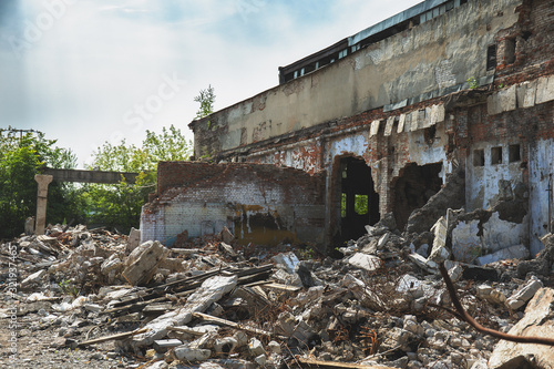 Ruined abandoned building with large pills of concrete garbage, aftermath of natural disaster or war, toned
