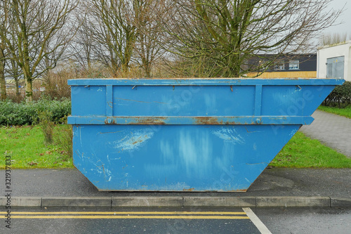 Blue color metal skip or dumpster in a street, selective focus. Concept renovation and construction job. Side view.