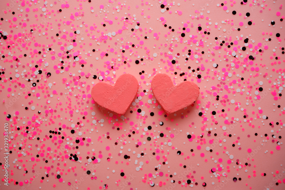 Two pink hearts on a pink background with confetti.