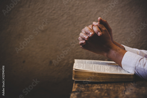 Hands folded in prayer on a Holy Bible in church concept for faith