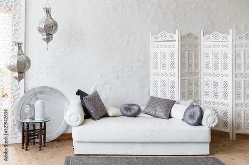 Eastern traditional interior. Romantic interior with comfortable authentic sofa. Exotic relaxation room. Arabic living room in white color with white sofa. White decorative wood panel on plaster wall