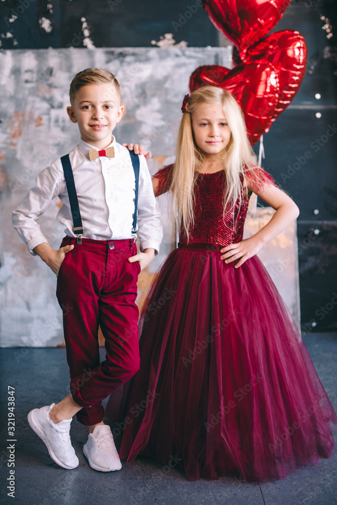 Happy little couple girl and boy with red hearts, red balloons, isolated on background. child boy and girl want to exchange hearts. St. Valentine's Day. Girl in luxury red dress. Happy little couple girl and boy with red hearts, red balloons, isolated on background. child boy and girl want to exchange hearts. St. Valentine's Day. Girl in luxury red dress.