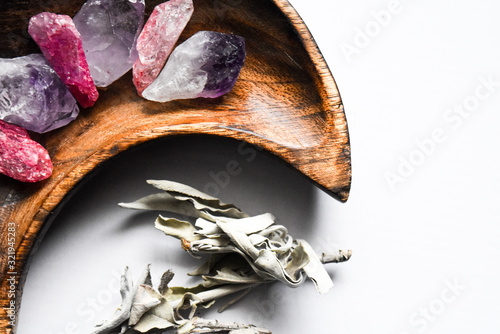 Pink and purple gemstones in a moon shaped dish with dried sage photo