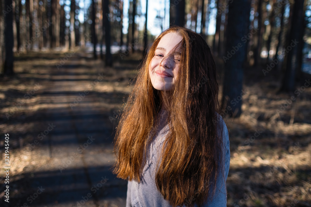 Obraz premium Portrait of cute girl with long bright red hair in the pine park.