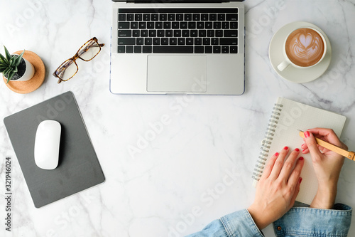 Flat lay workspace. Woman hand with coffee cup, smartphone, computer, notebook, planner and stationary with copy space on marble table background. Top view.