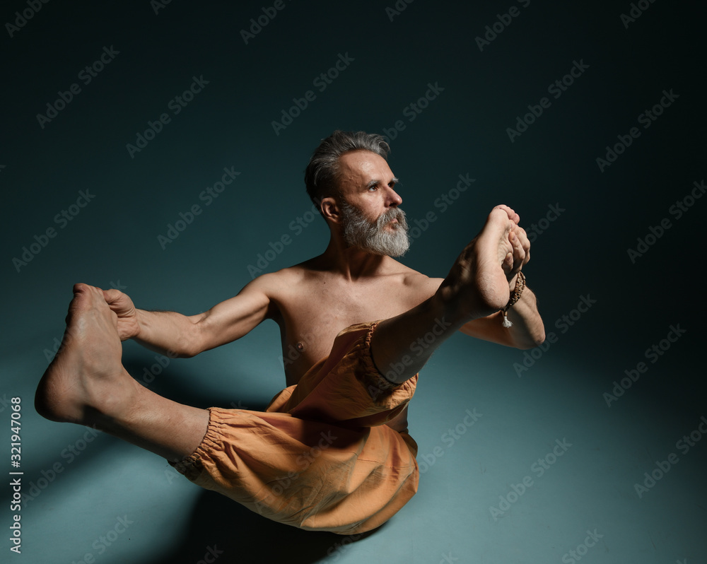 Obraz premium Old man with grey beard doing yoga, pilates, fitness training, stretching exercise, asana or balance workout on floor