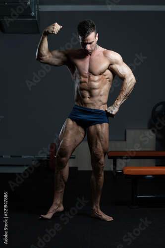 Bodybuilder Performing Front Biceps Pose In Gym
