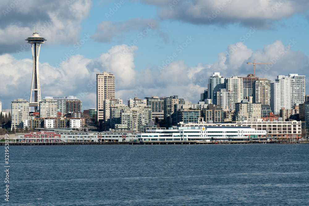 Downtown Seattle Skyline Cityscape Up Close from Puget Sound Water with Pier, Space Needle, Ferry Dock, and Boardwalk below Cloudy Sky as seen from Washington State Ferry