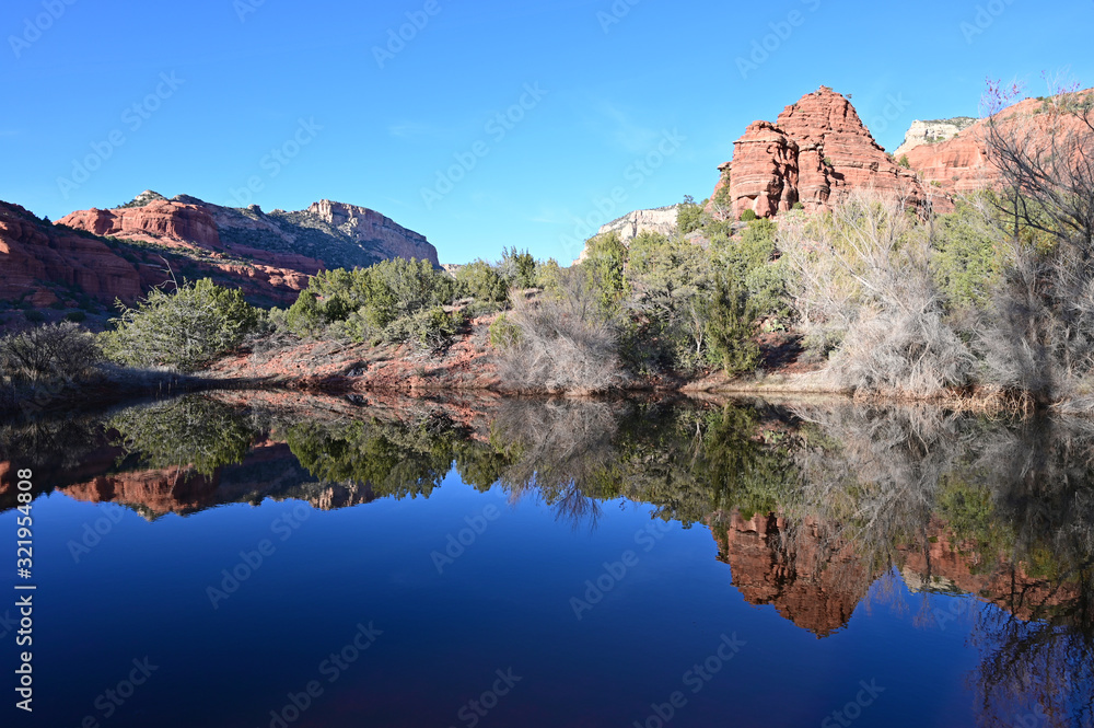 Red rock formations reflected in tranquil pond in Sedona, Arizona backcountry on clear cloudless winter afternoon.