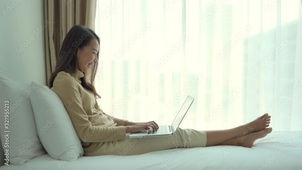 A young woman messaging friends online and working remotely using a laptop in bed. A young woman messaging friends online and working remotely using a laptop in bed.