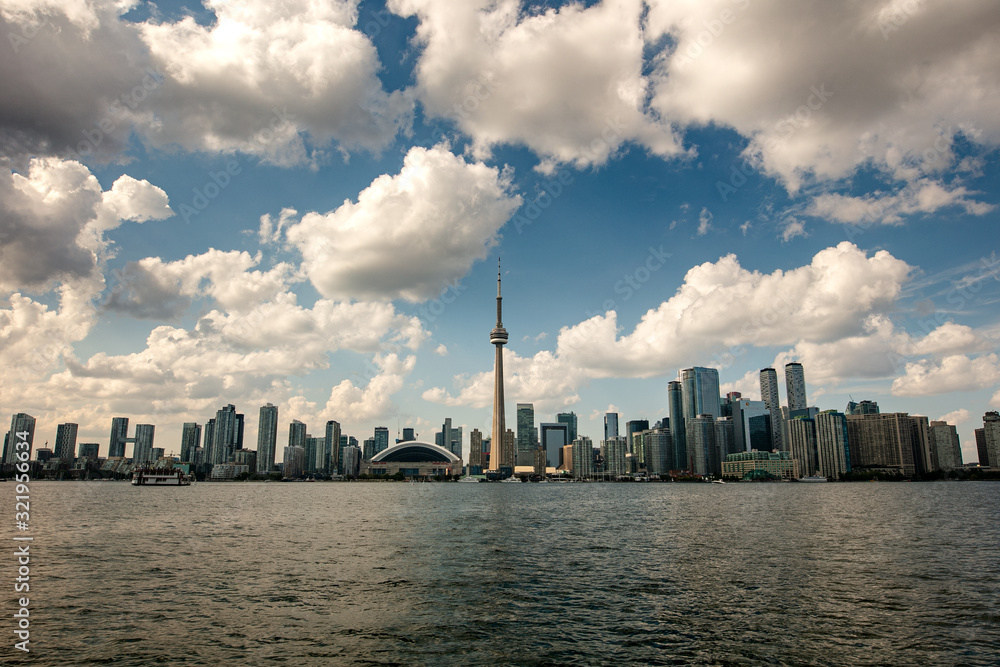 The skyline of Toronto, a view from the lake side - Toronto, Ontario, Canada. Panorama view of the Canadian city of Toronto, with white clouds on a blue sky with the Toronto tower. An urban view