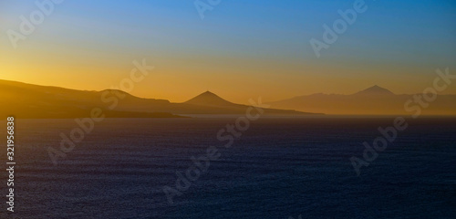 Spectacular sky colors and sunset landscape of a volcanic island with sun reflections in calm ocean.