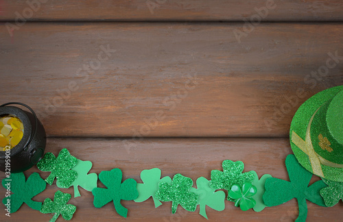 Saint Patrick's Day image of glittered and felt green sharmocks form a border on a rustic wooden background. A pot of Gold and a Leprchaun hat added..Copy space.