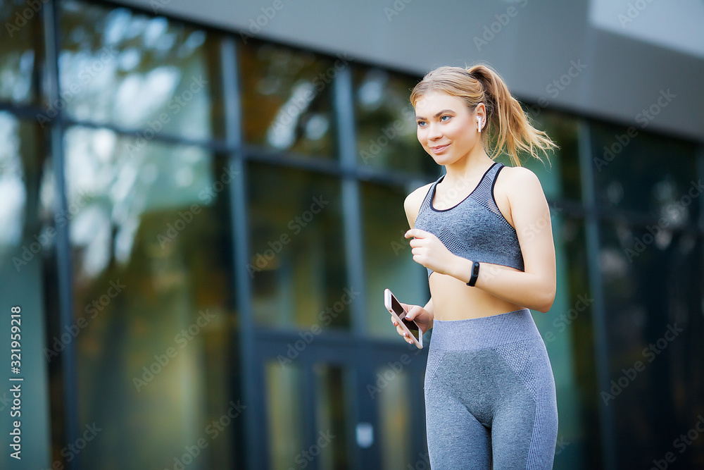 Photo of Joyful Fitness Woman 30s in Sportswear Touching Bluetooth Earpod and Holding Mobile Phone, While Resting in Green Park