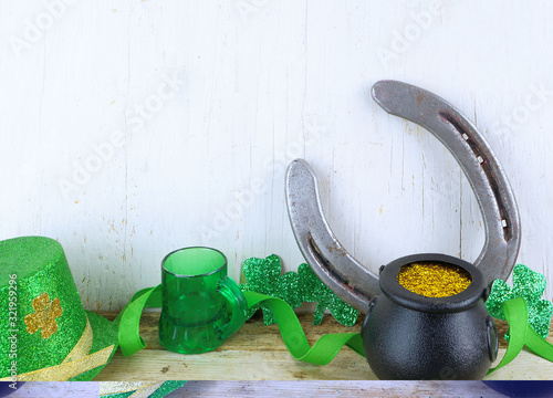 Saint Patrick's Day image of glittered green sharmocks, a horseshoe, a pot of gold dust and a leprechaun's hat on a rustic wooden background. Copy space.