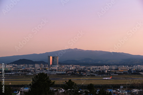The scenery of Jeju Island, which is dyed with the sunset light. The airport, the plane, Halla Mountain and the village can be seen at a glance.