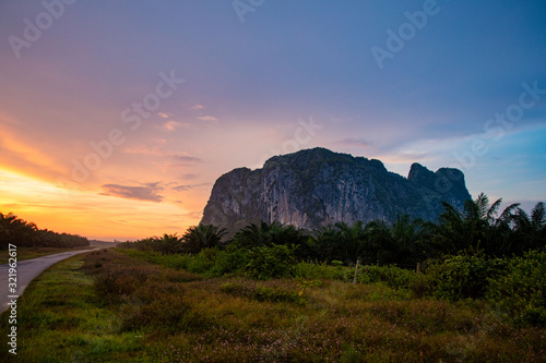 Sunrise at the Gua Charas Rock, Pahang, Malaysia. Sun is rising behind the rock or mountain. Red yellow sky of rising sun, palm trees in front of the scenic morning view. Located at Pahang, Malaysia