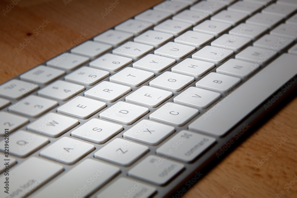 Close up of a white aluminum keyboard on a wooden desk. Macro photography of a wireless computer keyboard. White keys on a silver frame. Detailed shot of a modern computer keyboard on wood Close up of a white aluminum keyboard on a wooden desk. Macro photography of a wireless computer keyboard. White keys on a silver frame. Detailed shot of a modern computer keyboard on wood