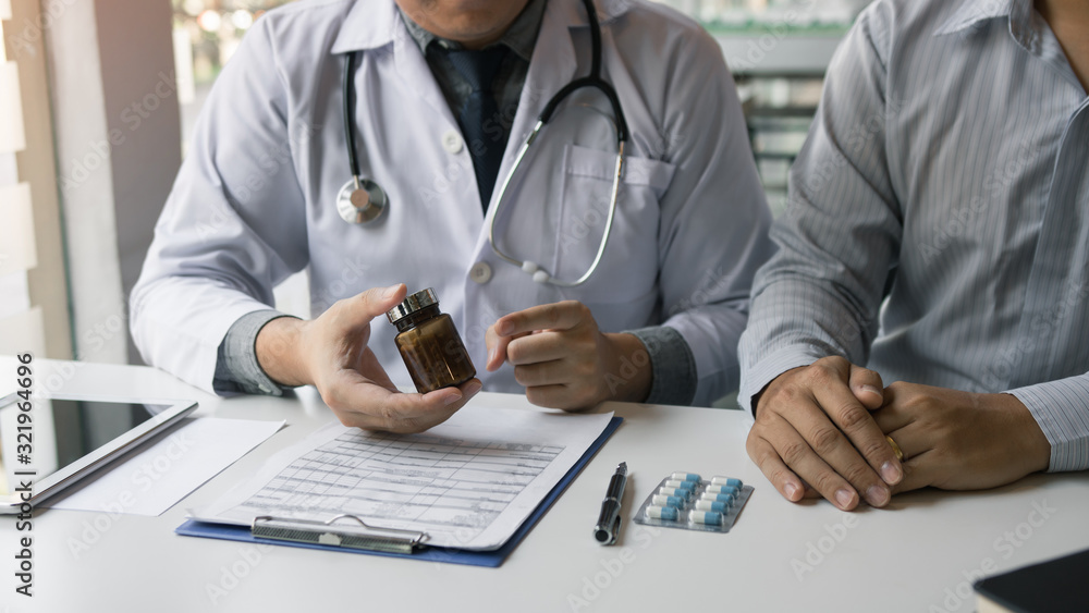 Fototapeta premium Confident doctor man holding a pill bottle and writing while talking with senior patient and reviewing his medication at office room.