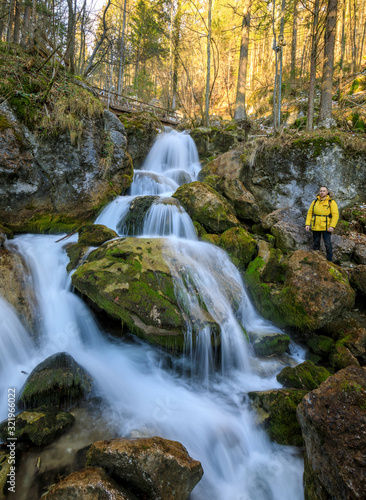 Fototapeta Naklejka Na Ścianę i Meble -  hiker in yellow rain jacket standing in front of waterfall on a moody day in Austria