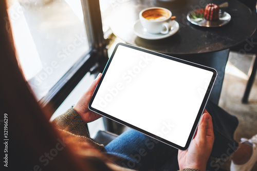 Mockup image of a woman holding black tablet pc with blank white screen in cafe