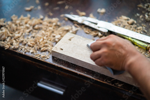 Wood shavings carpenter working with a metal spokeshave and a blurry background. Light beige colored poplar wood with slight curves in it. Vintage woodworking, handwork, handmade