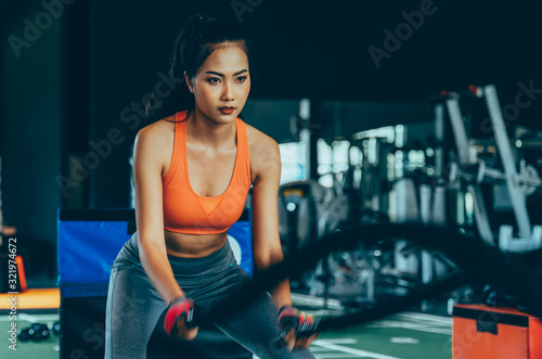 Asian mixed female bodybuilder practicing crossfit battle ropes with motion at fitness gym. Determination and concentration concept