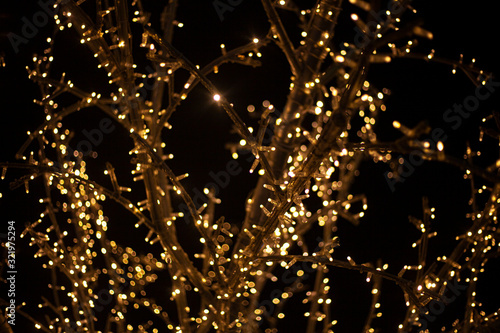 A tree decorated with garlands. Christmas light bulbs on twigs. LED lights shine with a warm yellow light. Festive background for a cozy atmosphere.
