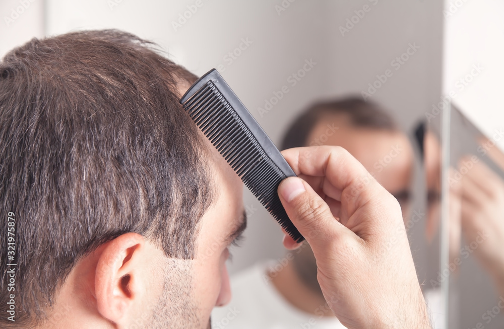 Caucasian man holding comb in bathroom.