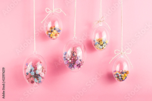 Easter eggs are transparent and filled with small colorful flowers hanging on a rope on a pink background. Minimalistic holiday decoration. photo