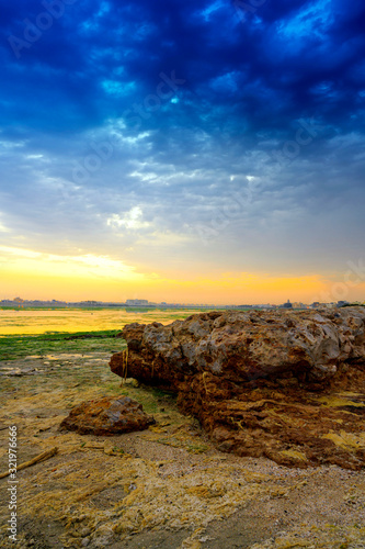 Rusty dirty big broken rock on the beach over colorful sunrise sky background, Bahrain.