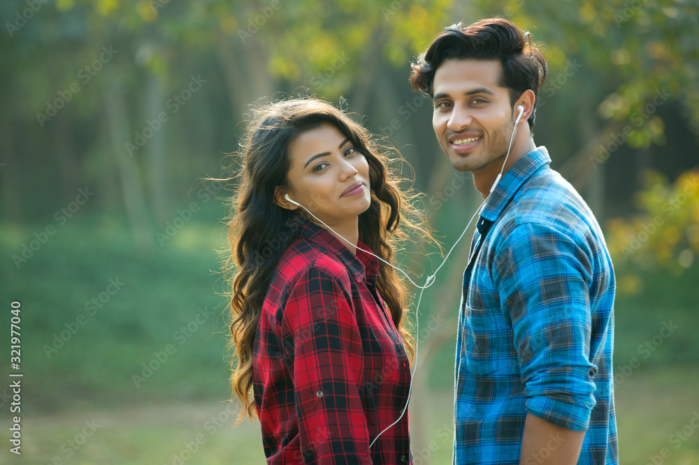 Young couple standing in a garden sharing an earphone listening to music. Young couple standing in a garden sharing an earphone listening to music.