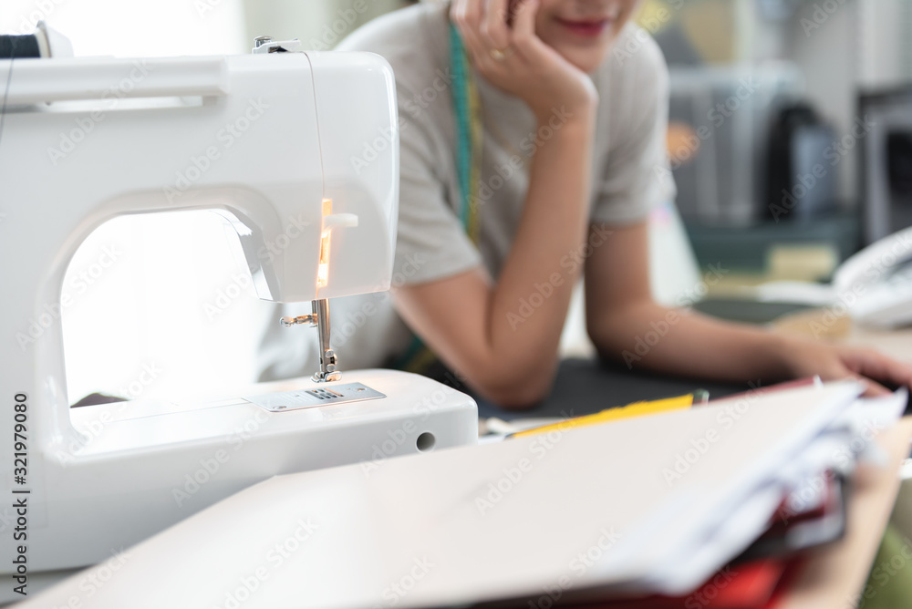 Close up. Desk of Woman Tailor with sewing machine while working and thinking propped up the head about pattern of the garment. Business design tailor in the home office concept.