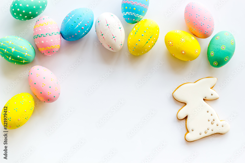 Easter symbols. Painted eggs and bunny gingerbread on white desk top-down frame copy space