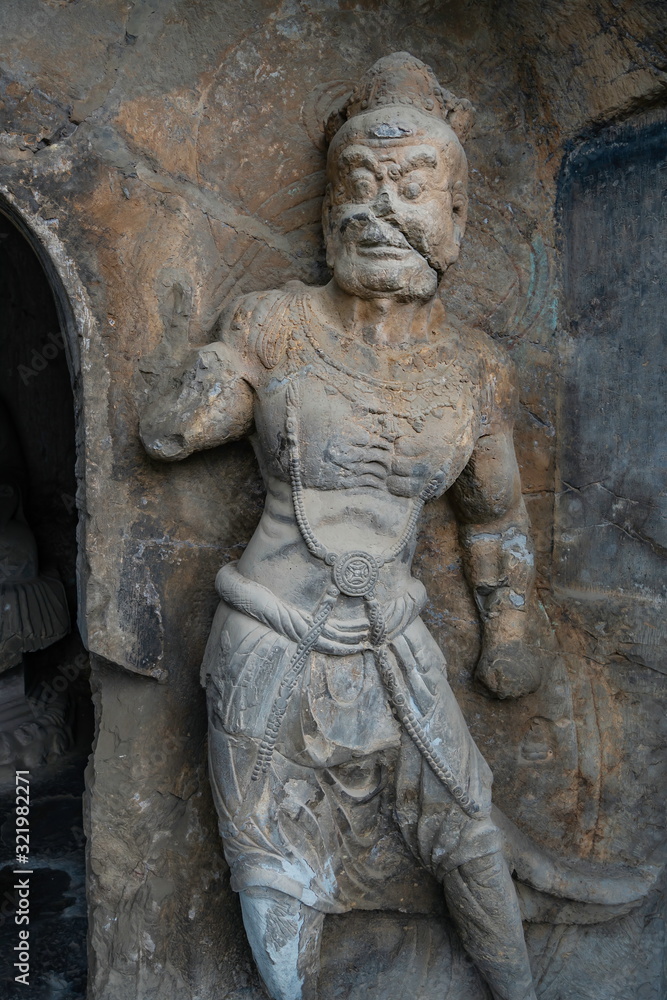 Muscular warrior carved in limestone. Figure is protecting a cave door.  Wei style grotto at Longmen Grottoes, Luoyang, Henan province, China