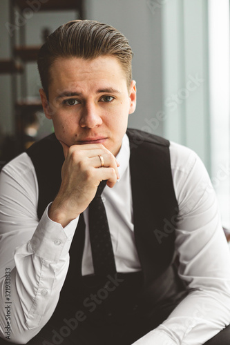Portrait of a young successful businessman in a suit in the office. Close-up sitting in a chair by the window