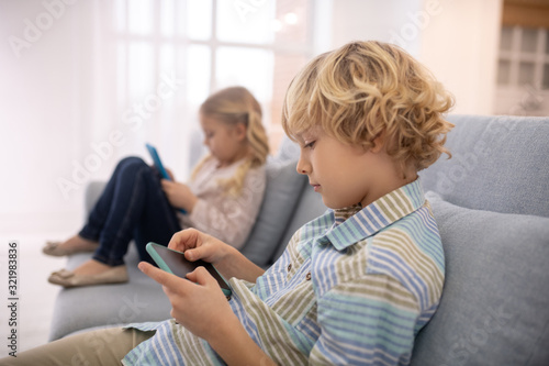 Boy and girl sitting on sofa and playing with gadgets